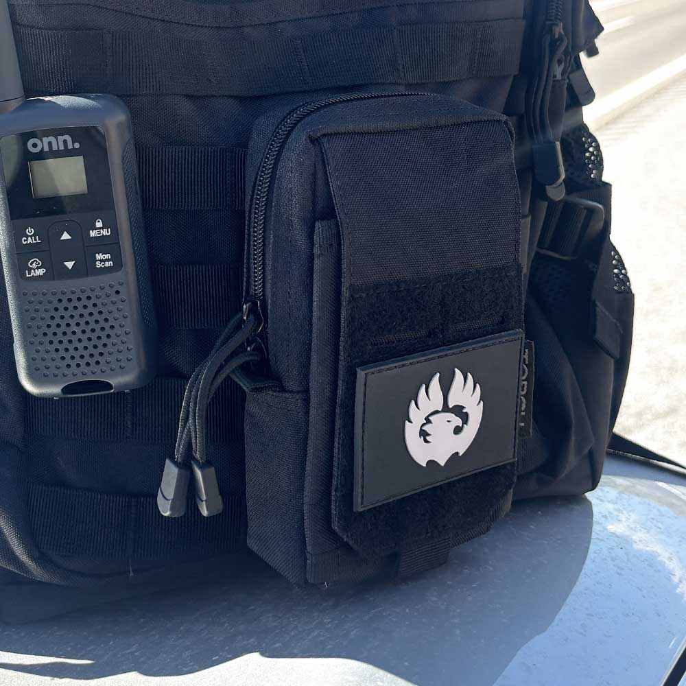 Close-up of TORCH EDC Admin Pouch black shown outdoors attached to backpack for hiking or travel use.